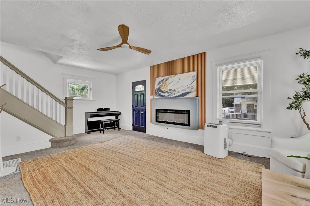 732 Carpenter Street Akron, OH 44310 - Photo 9 of 38 Carpeted living room with a textured ceiling, a ceiling fan, stairway, and a glass covered fireplace
