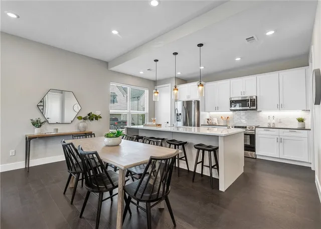 a kitchen with stainless steel appliances a dining table chairs stove refrigerator and cabinets