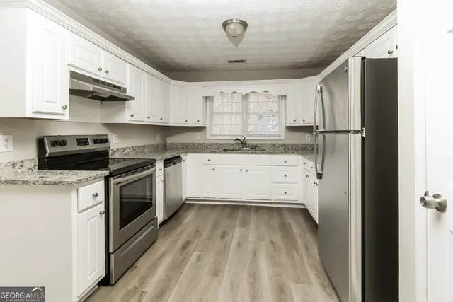 a kitchen with granite countertop a sink stainless steel appliances and white cabinets