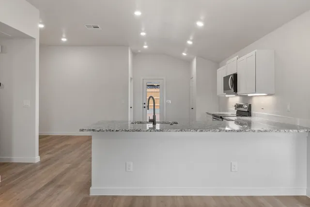 a view of a kitchen with granite countertop a sink and dishwasher a stove top oven with wooden floor