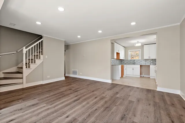 an empty room with wooden floor and kitchen view