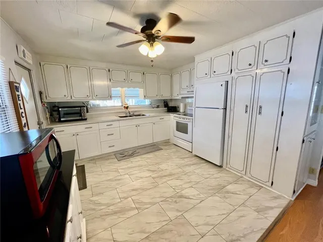 a kitchen with granite countertop a refrigerator a stove a sink dishwasher and white cabinets with wooden floor