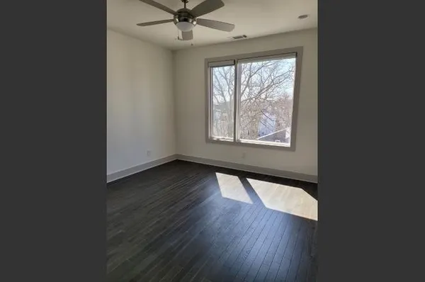 an empty room with wooden floor chandelier fan and windows