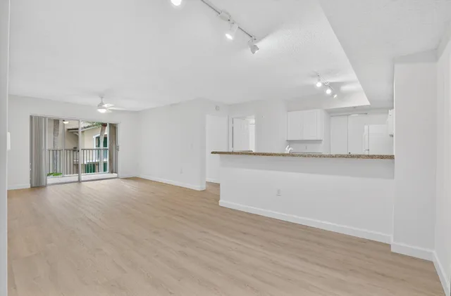 a view of an empty room with wooden floor and kitchen