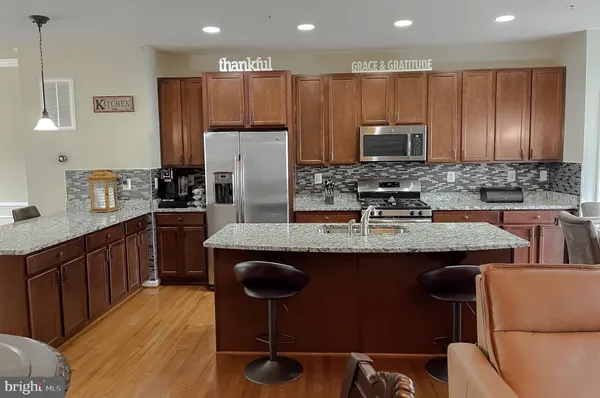 a kitchen with stainless steel appliances granite countertop a stove a refrigerator a kitchen island a dining table and chairs