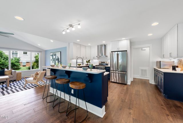 a kitchen with stainless steel appliances granite countertop a refrigerator a sink dishwasher a dining table and chairs with wooden floor