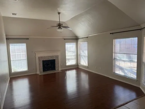 an empty room with wooden floor fireplace and windows