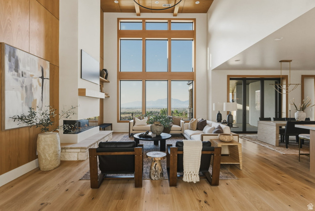 923 North Emery Lane Elk Ridge, UT 84651 - Photo 11 of 101 Two-story living area featuring extensive window walls, wood-finish flooring, a linear fireplace with stone hearth, a wood-paneled accent wall, and a wood-slat ceiling with exposed beams