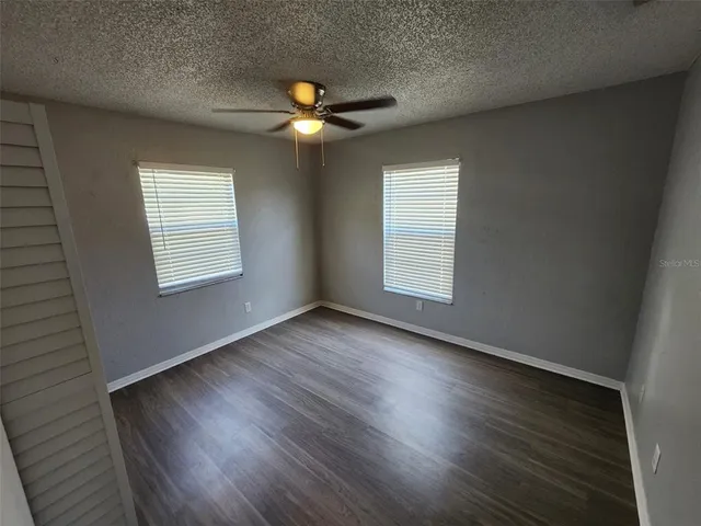 an empty room with wooden floor fan and windows