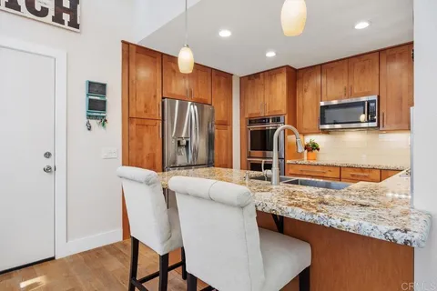 a kitchen with stainless steel appliances granite countertop a refrigerator a stove a sink a dining table and chairs with wooden floor