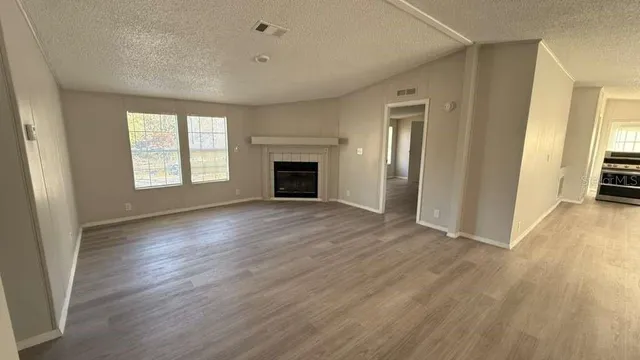 an empty room with wooden floor fireplace and windows