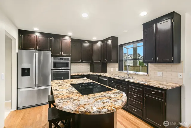 a kitchen with stainless steel appliances kitchen island granite countertop a sink a stove and refrigerator