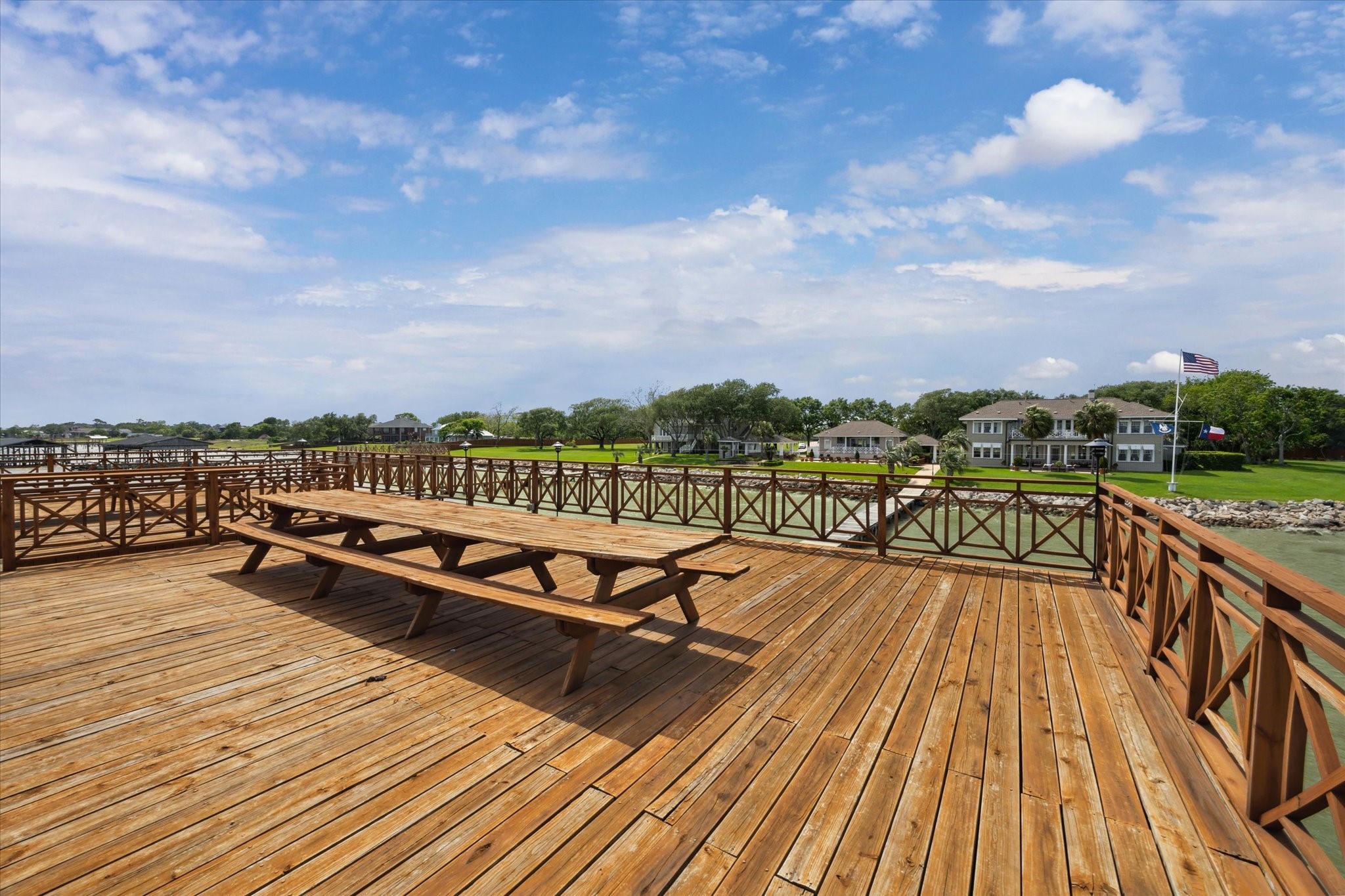 102 South R Street La Porte, TX 77571 - Photo 20 of 43 Expansive wooden deck overlooking a serene waterfront with a picnic table and views of nearby homes, perfect for outdoor relaxation and gatherings.