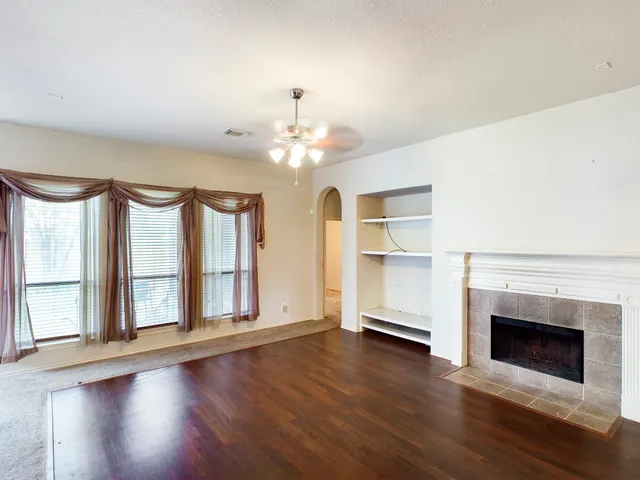 an empty room with wooden floor fireplace and windows