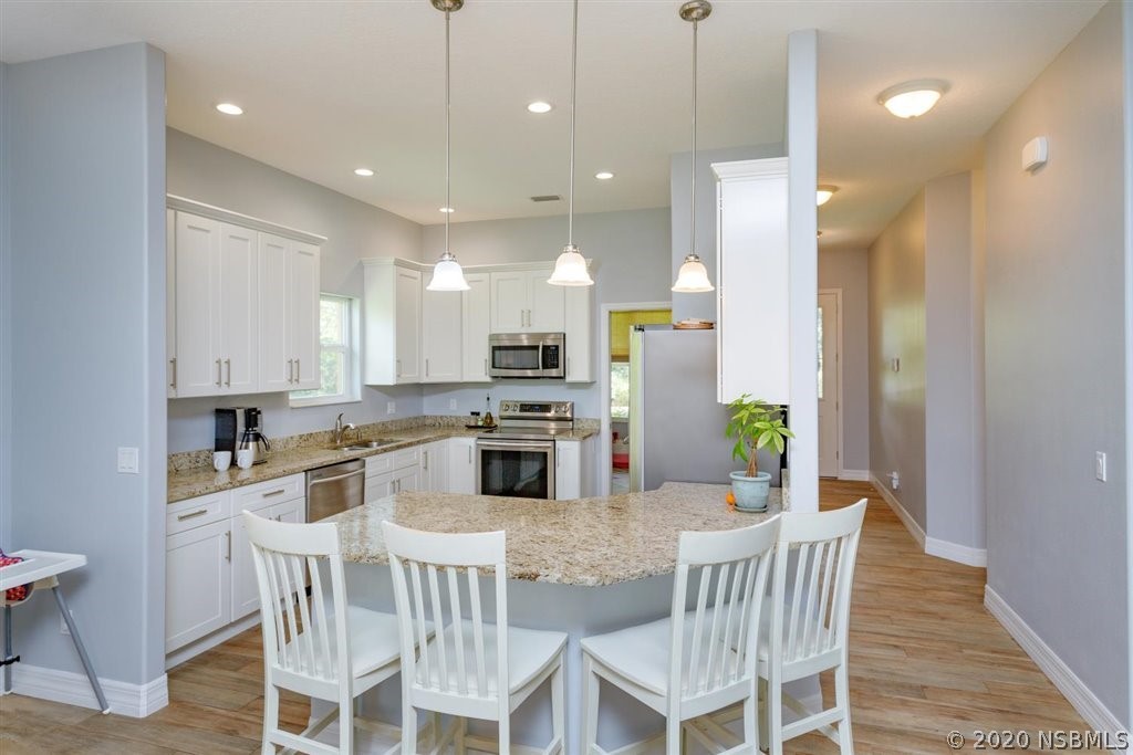 141 Poinciana Road Edgewater, FL 32141 - Photo 4 of 26 a kitchen with stainless steel appliances kitchen island granite countertop a dining table chairs and white cabinets
