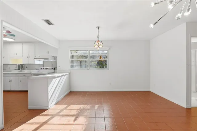 a view of an empty room with kitchen and chandelier