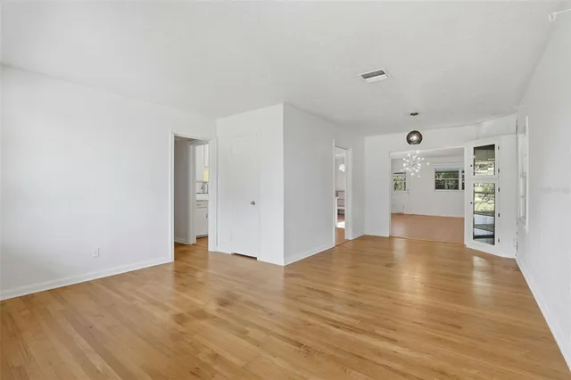 a view of an empty room with wooden floor and a kitchen