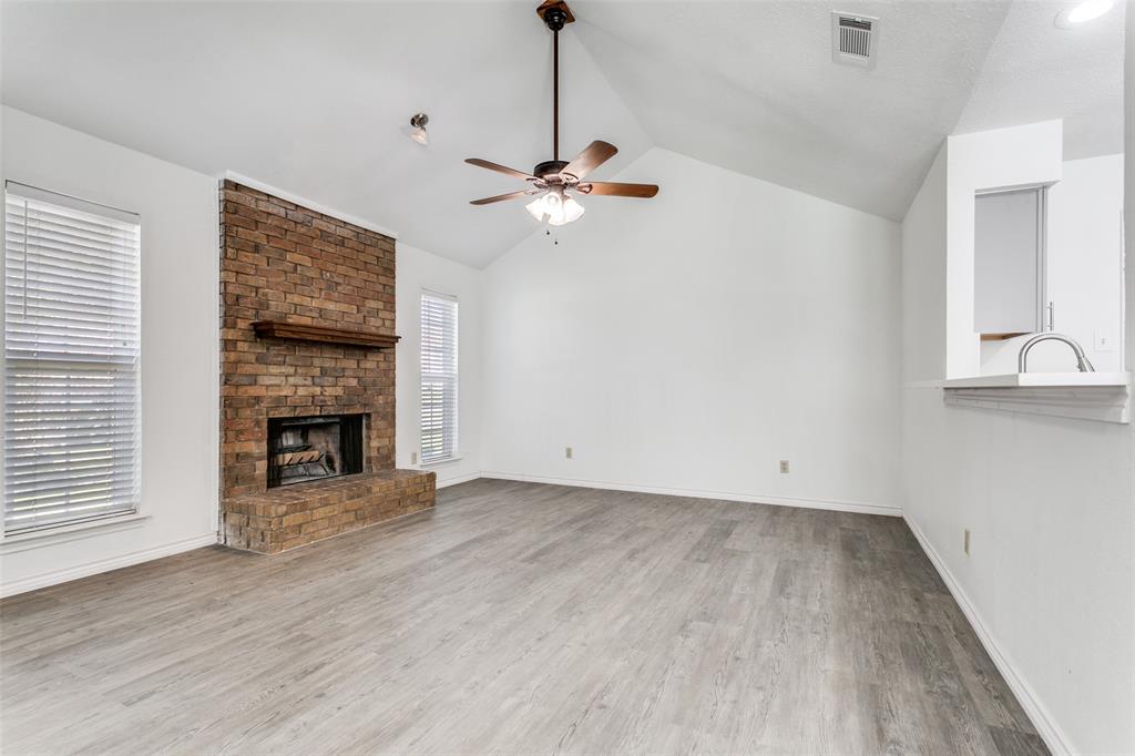 2121 Stone Moss Lane Grapevine, TX 76051 - Photo 3 of 12 Living room featuring ceiling fan hanging from cathedral ceiling, brick wood- burning fireplace, and rustic, hand-scraped look luxury vinyl plank.