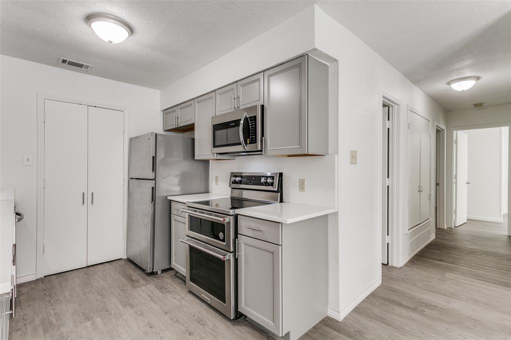2121 Stone Moss Lane Grapevine, TX 76051 - Photo 7 of 12 Kitchen with gray cabinetry, stainless steel appliances, white quartz countertops and the double doors lead to the laundry room with room for a regular size washer and dryer