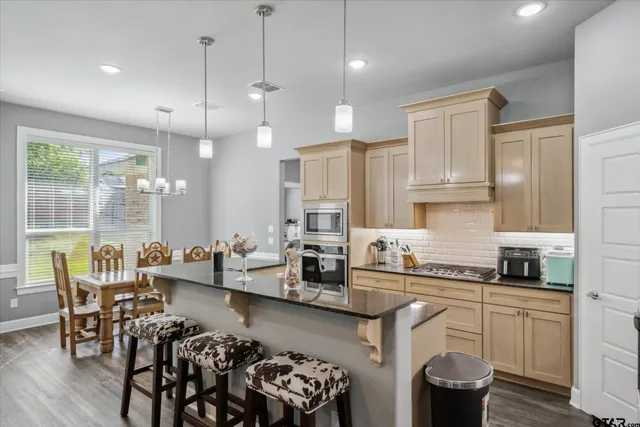 a kitchen with stainless steel appliances granite countertop a stove a sink a dining table and chairs with wooden floor