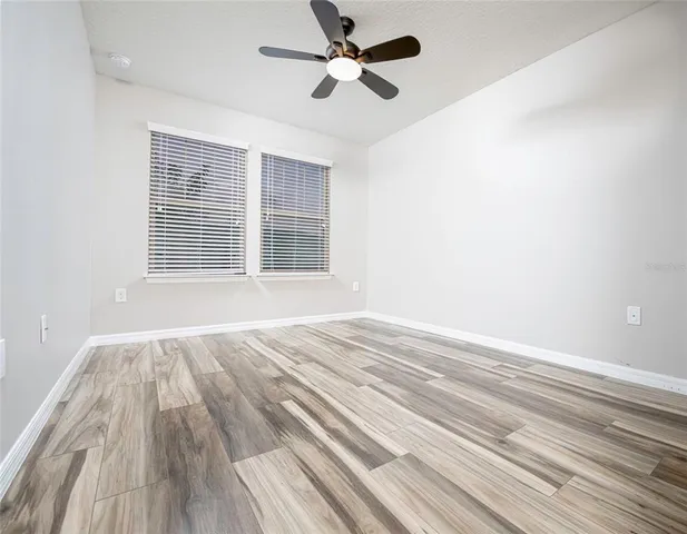an empty room with wooden floor ceiling fan and windows
