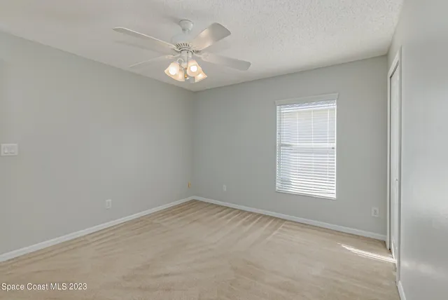 an empty room with a chandelier fan and windows