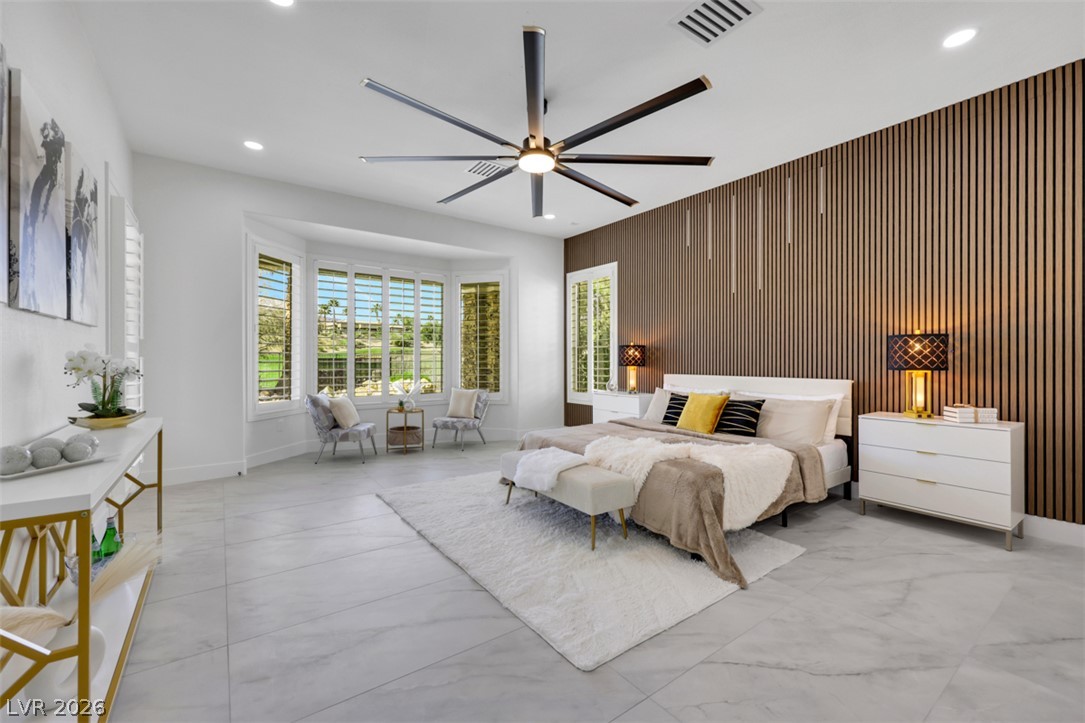 5015 Rivedro Street Las Vegas, NV 89135 - Photo 50 of 91 A spacious primary bedroom features a striking accent wall, a bay window with a seating area, and a large ceiling fan.