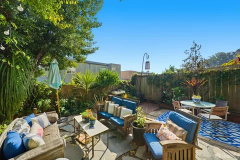 a backyard with table and chairs potted plants and a large tree