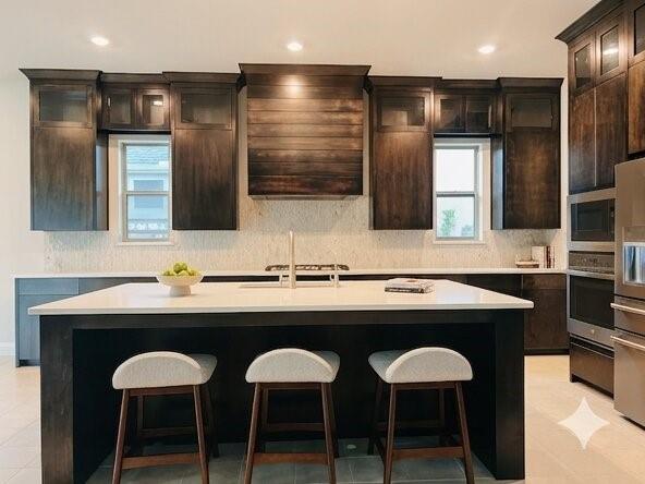 6825 Entwistle Road Frisco, TX 75034 - Photo 4 of 25 The kitchen features a spacious island with a white countertop, dark wood cabinetry, stainless steel appliances, and recessed lighting