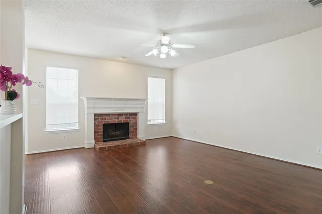 a view of an empty room with wooden floor fireplace and a window