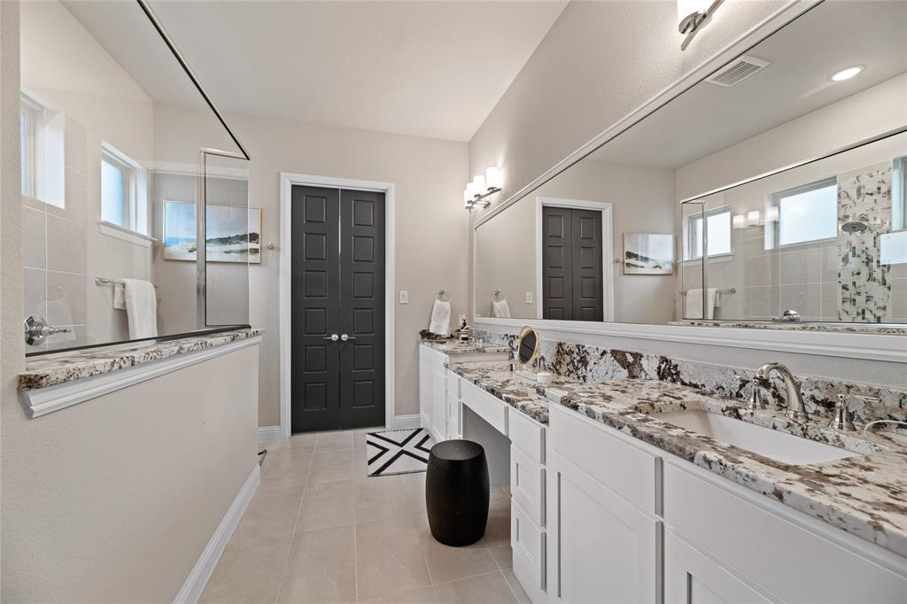 2262 Poppyvine Road Frisco, TX 75033 - Photo 20 of 40 Bathroom featuring a dual vanity with granite countertops, light-colored tile flooring, a large wall-mounted mirror, and a glass-enclosed shower