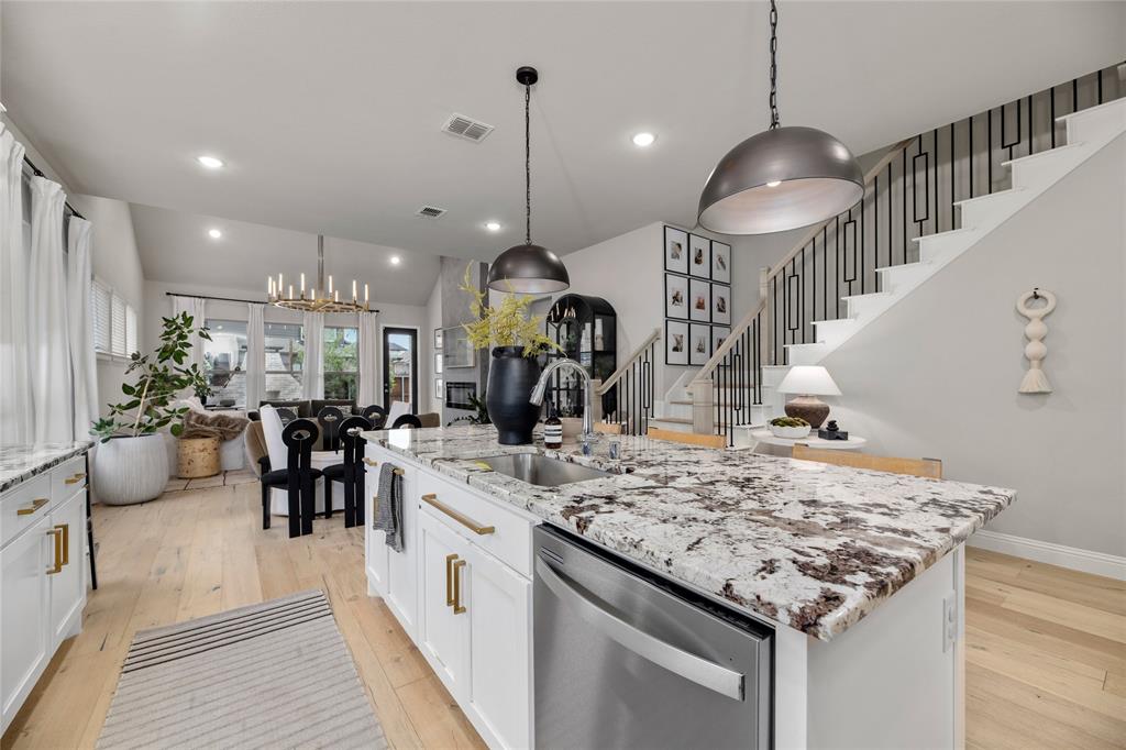 2262 Poppyvine Road Frisco, TX 75033 - Photo 6 of 40 The kitchen features white cabinetry with gold-toned hardware, a stone countertop, and an integrated stainless steel dishwasher