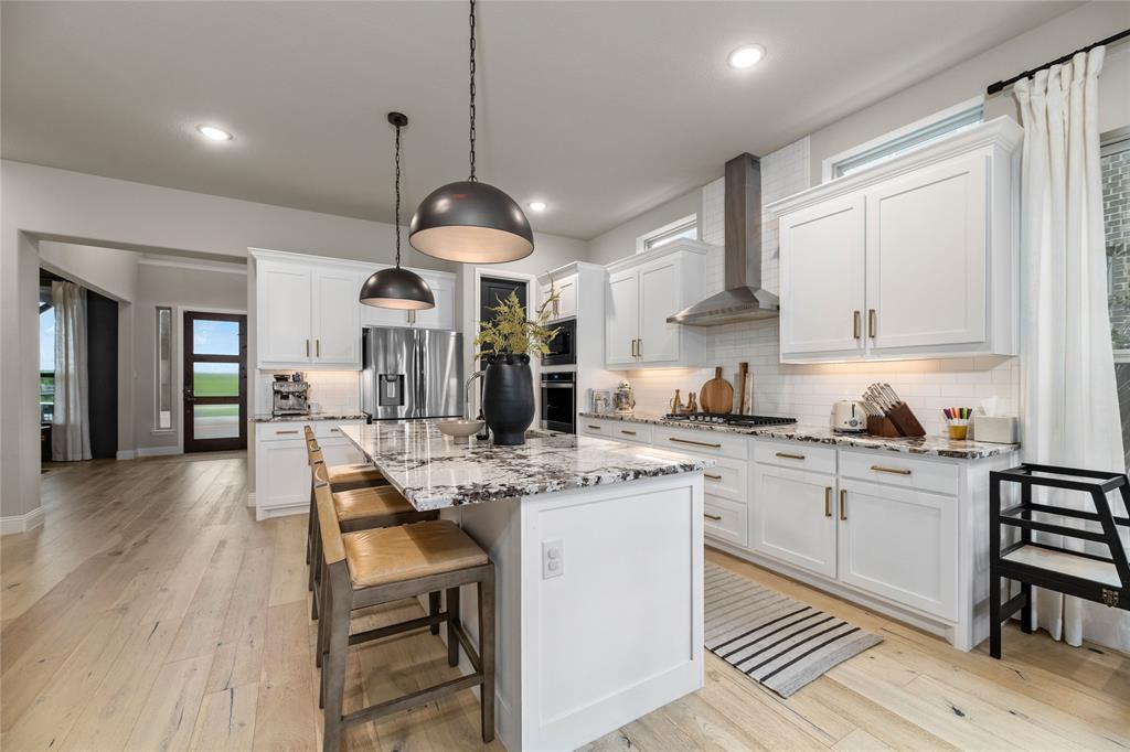 2262 Poppyvine Road Frisco, TX 75033 - Photo 7 of 40 The kitchen features white cabinetry, stone countertops, a large island with seating, stainless steel appliances, and light wood flooring