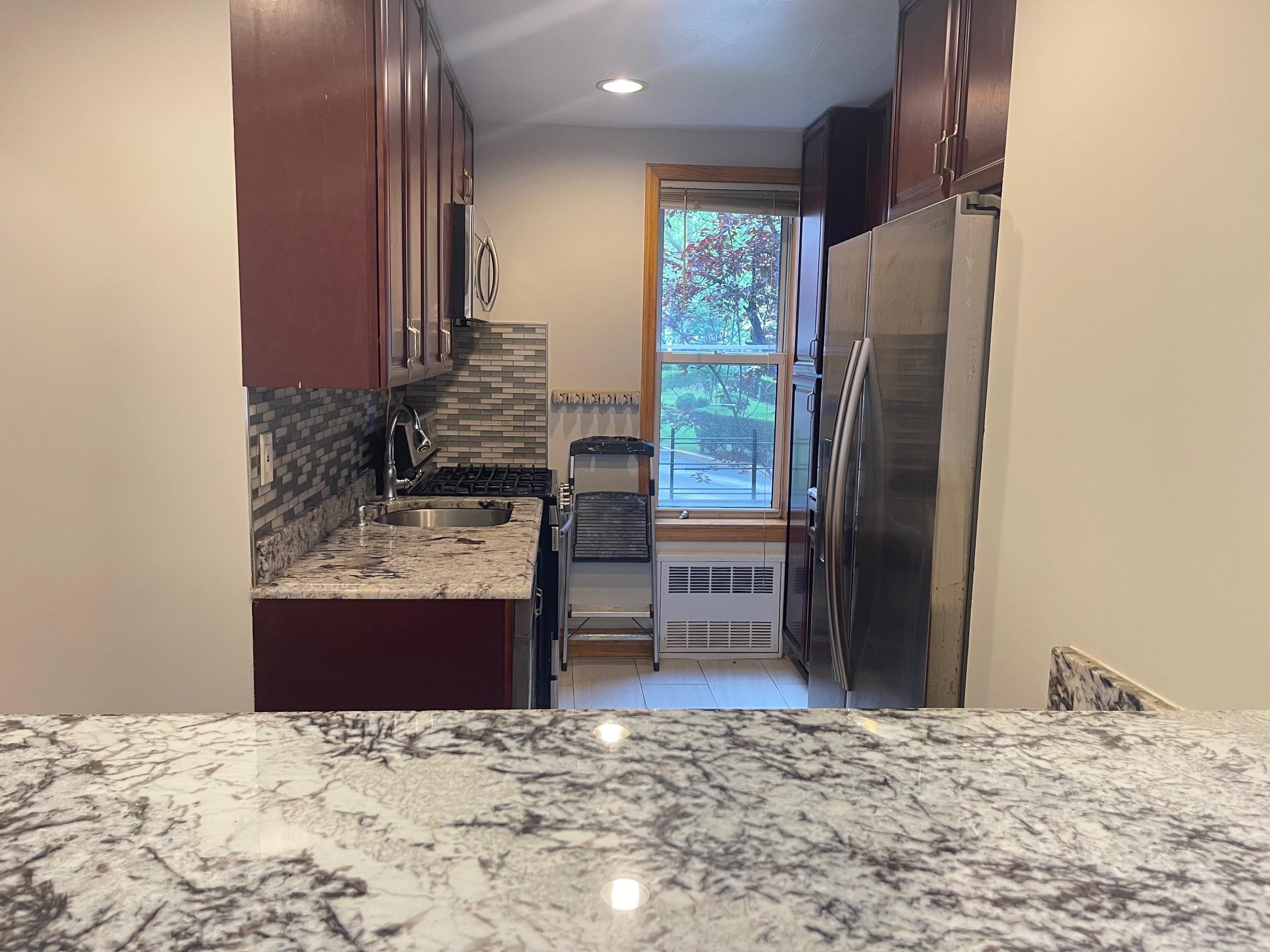 59-30 108th Street, Unit 2JJ Queens, NY 11368 - Photo 9 of 15 Kitchen featuring appliances with stainless steel finishes, radiator heating unit, backsplash, light tile patterned floors, and light stone counters