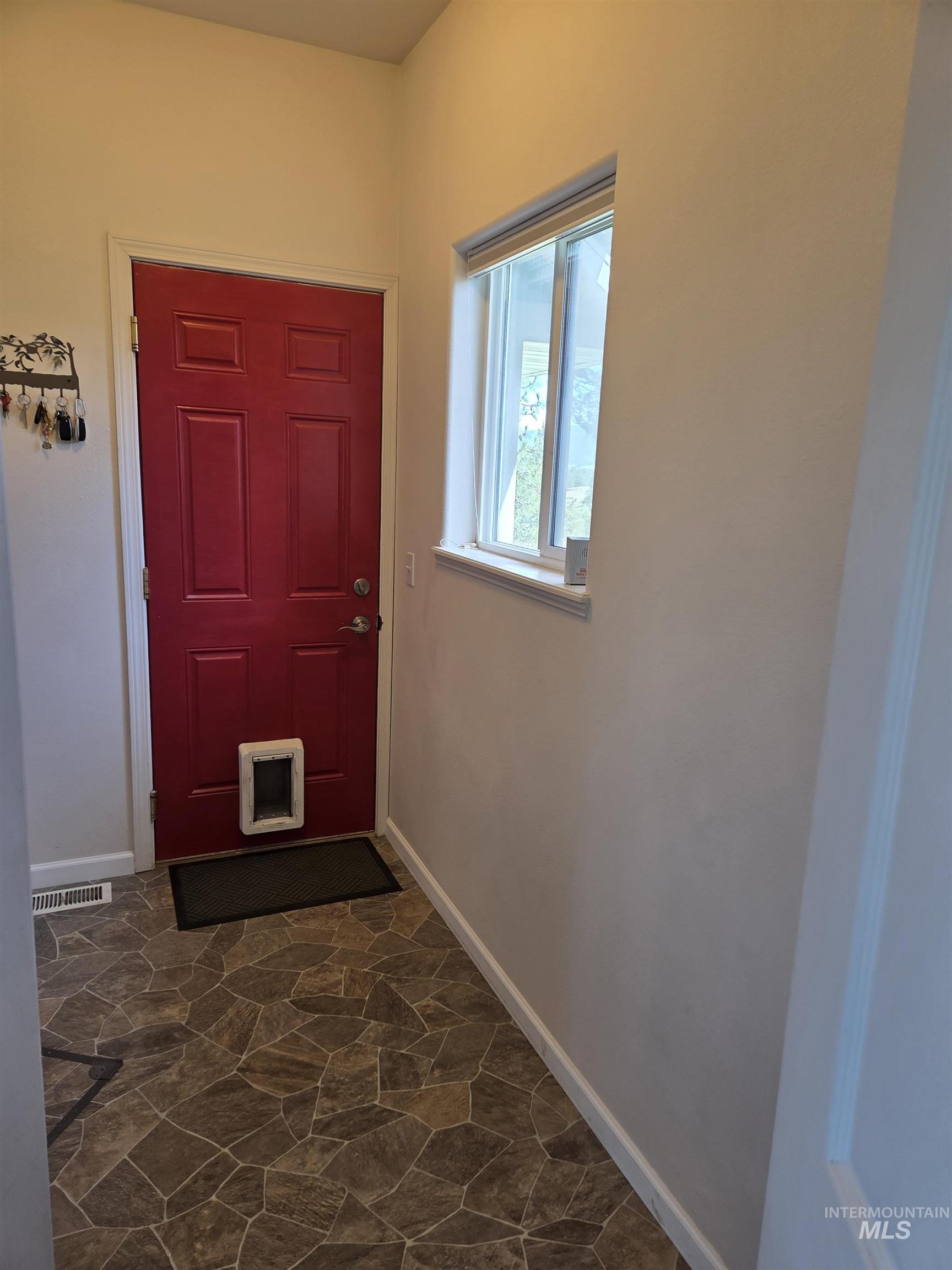 1085 Wallen Road Moscow, ID 83843 - Photo 31 of 50 Entryway featuring a red paneled door with white trim, a large window, patterned floor tile, and white baseboards