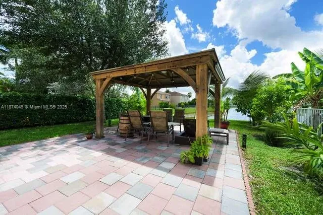 a view of a patio with table and chairs under an umbrella with large trees