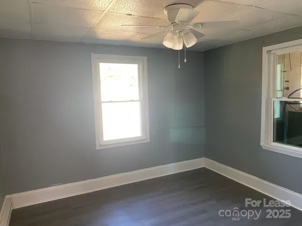 an empty room with wooden floor fan and windows