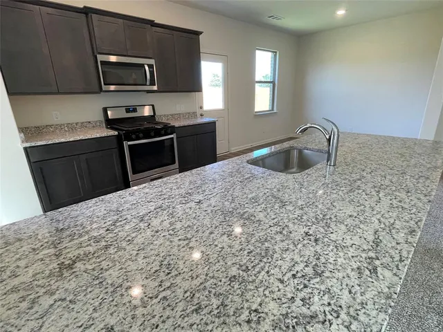 a kitchen with stainless steel appliances granite countertop a sink stove microwave and refrigerator