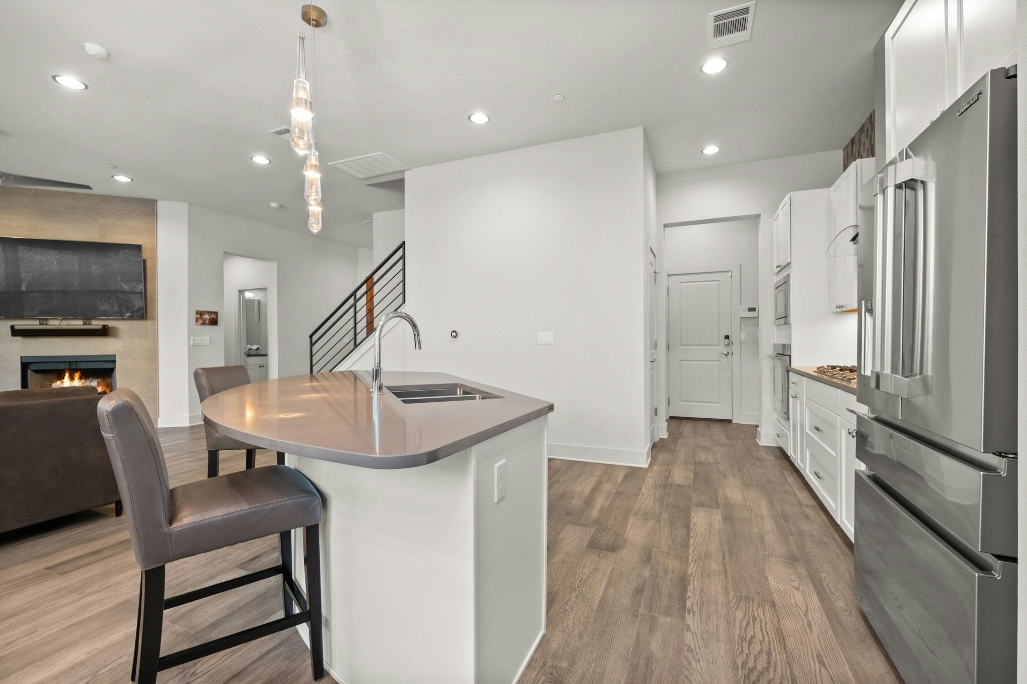 8110 Ranch Road 2222, Unit 92 Austin, TX 78730 - Photo 8 of 40 Open-concept kitchen and living area featuring wood-finish flooring, a contemporary kitchen island with an undermount sink, stainless steel appliances, and a modern fireplace with a stone surround