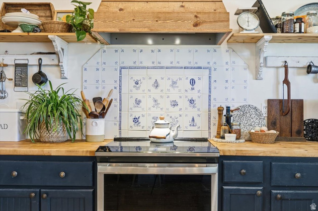 1634 West Arimo Road Arimo, ID 83214 - Photo 10 of 89 Kitchen featuring a built-in stainless steel electric range, butcher block countertops, custom painted cabinetry with decorative hardware, a white and blue patterned tile backsplash, and a wood range hood