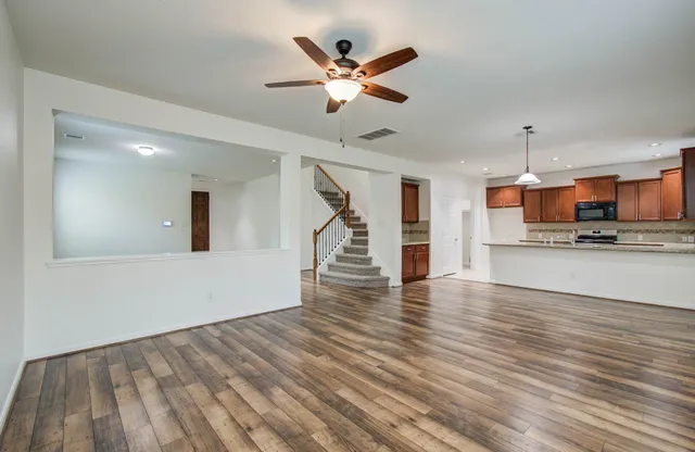 a view of an empty room and kitchen with wooden floor and a ceiling fan