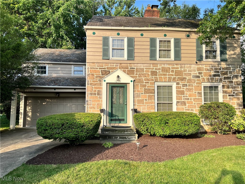 View of front of house featuring concrete driveway, a chimney, an attached garage, stone siding, and roof with shingles