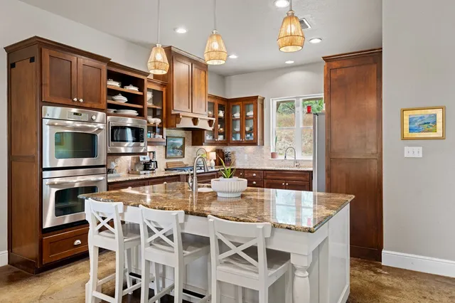 a kitchen with stainless steel appliances kitchen island granite countertop a refrigerator a stove top oven and a dining table with wooden floor