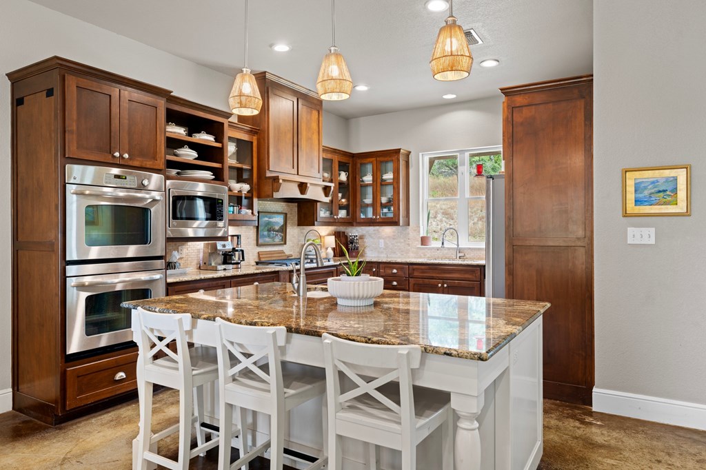 151 Kerr Canyon Pass South Kerrville, TX 78028 - Photo 6 of 45 a kitchen with stainless steel appliances kitchen island granite countertop a refrigerator a stove top oven and a dining table with wooden floor
