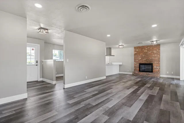 an empty room with wooden floor fireplace and windows