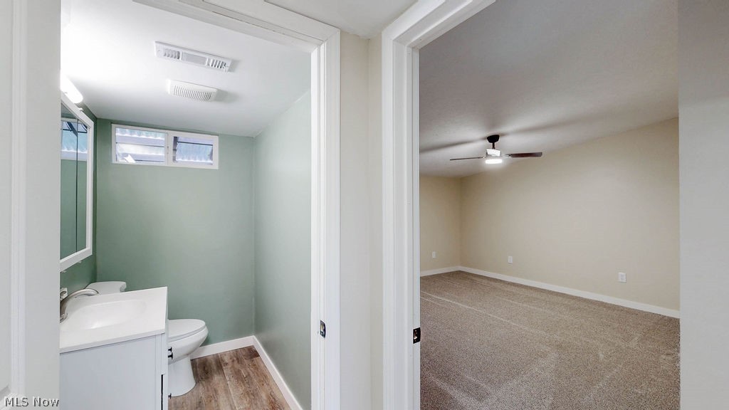 18620 Shaw Road Chagrin Falls, OH 44023 - Photo 14 of 44 Powder room with a modern vanity and wood-finish flooring, accompanied by a spacious room featuring carpeting and a ceiling fan