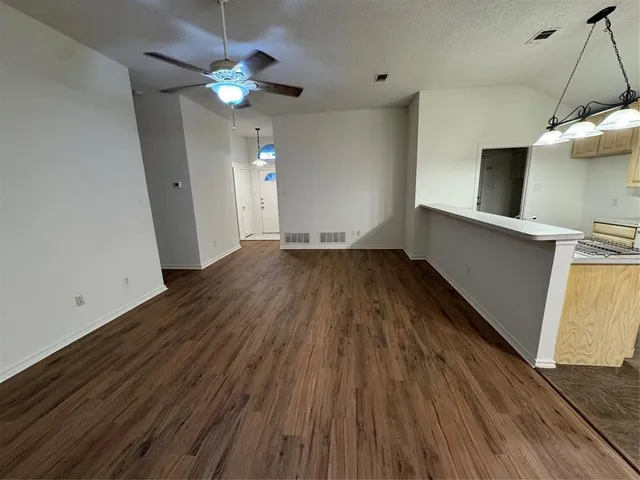 a view of an empty room with wooden floor and a ceiling fan