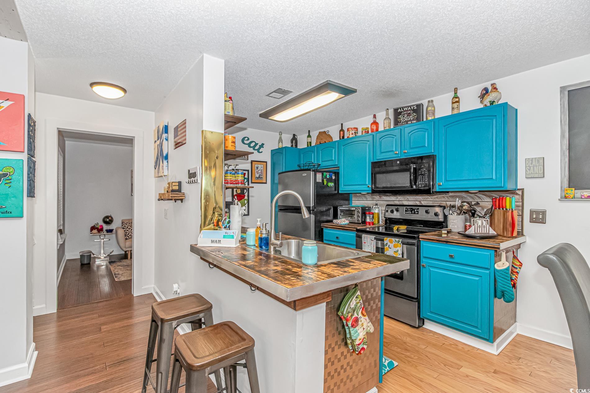 4394 Daphne Lane, Unit G Murrells Inlet, SC 29576 - Photo 12 of 30 Kitchen featuring stainless steel appliances, a kitchen bar, light wood-style floors, a textured ceiling, and decorative backsplash