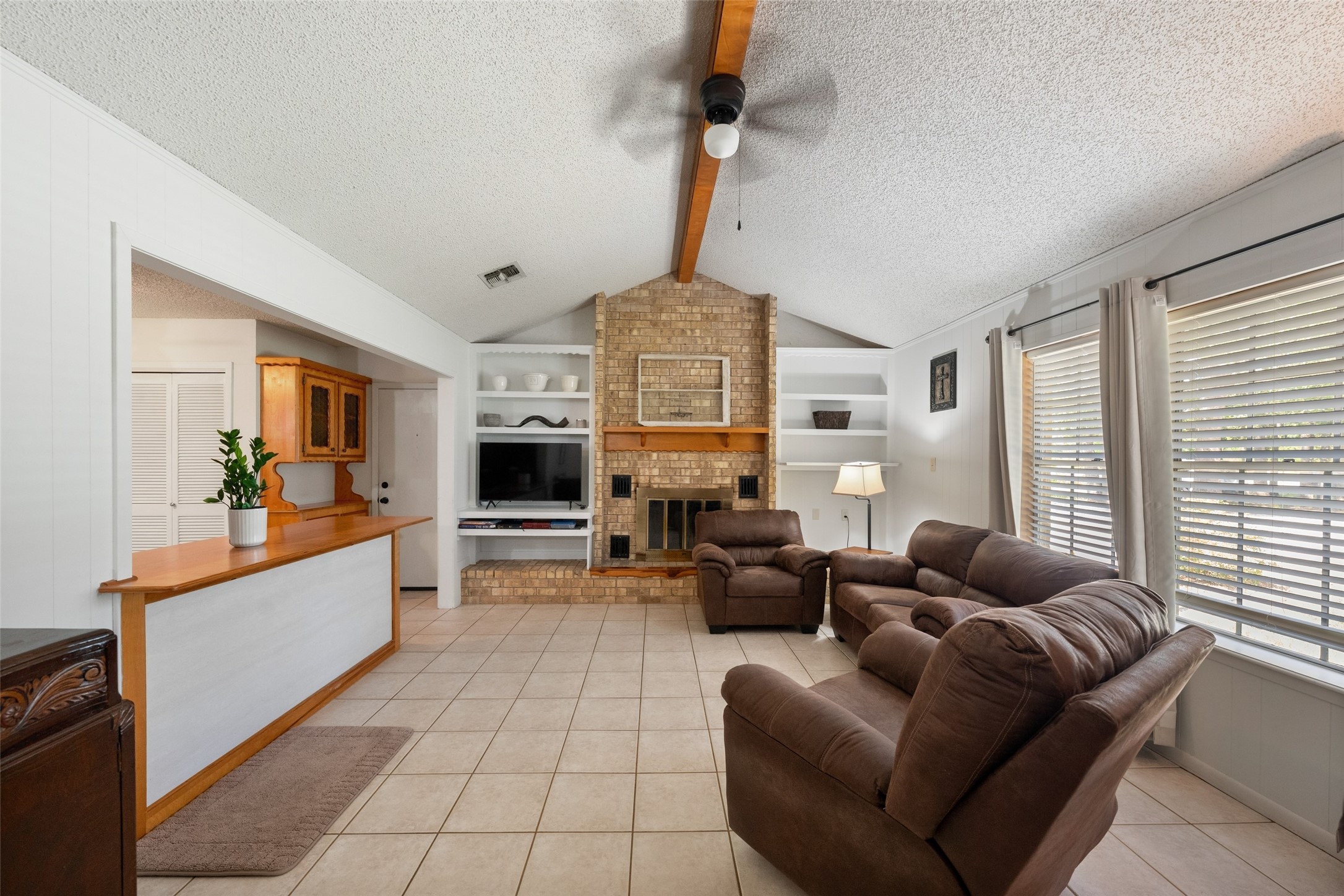 25739 Old Howth Road Hempstead, TX 77445 - Photo 5 of 36 A classic brick wood-burning fireplace and built-in shelving create a warm focal point, while the open pass through keeps the living room connected to the kitchen and dining area.