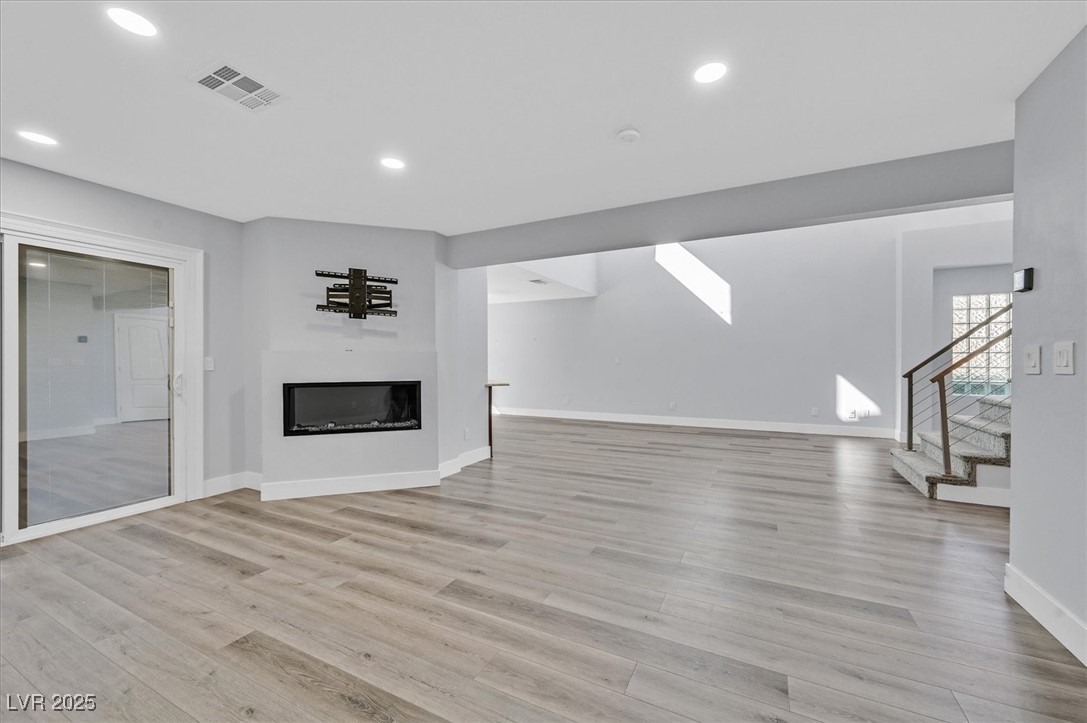 5421 Painted Mirage Road Las Vegas, NV 89149 - Photo 5 of 35 Unfurnished living room featuring light wood-type flooring, a glass covered fireplace, visible vents, and stairway